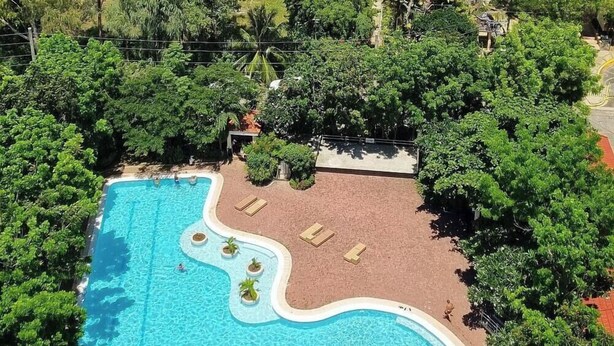 A view from the balcony of a hotel with a swimming pool, lush greenery, and a view of the ocean. - Huge Lux. 2 BR Condo (100 SQM)  2 pools - Beach, Sea-views, Gym, Tours available (Lapu-Lapu City)
