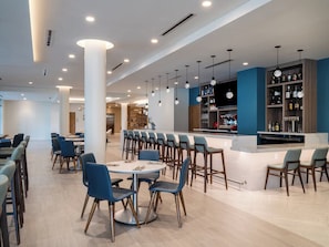 Un vestíbul d'hotel modern amb taules i cadires rodones, una zona de bar i una àrea d'estar amb vista a l'interior.