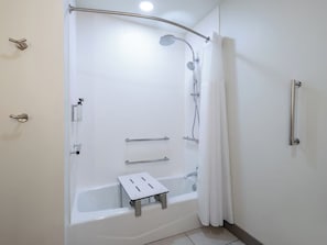 Ein modernes Badezimmer mit bodenebenen Dusche, Haltegriffen, Duschbrause und einer weißen Badewanne.