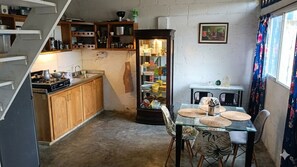 Cocina compacta con armarios de madera, estufa a gas y comedor con mesa y sillas de vidrio.
