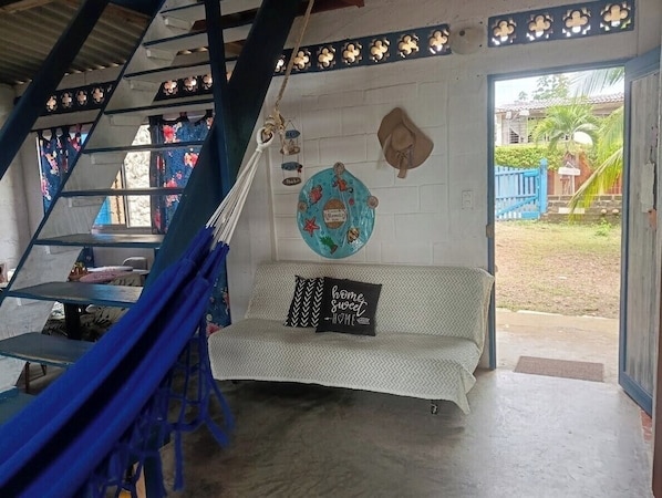 A room with a staircase, a sofa with a cushion, a wall with a decorative plate, and a view of the outside.