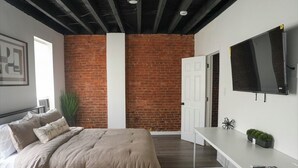 Un dormitorio con cama, escritorio, televisor y pared de ladrillo.