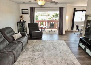 A living room with a sofa, a chair, a TV, and a balcony with a table and chairs. - Gorgeous 2-bedroom condo with AC in Long Beach two garages (Long Beach)