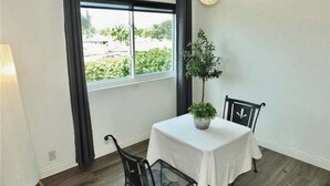 A room with a table, chairs, a potted plant, a window, and a lamp. - Gorgeous 2-bedroom condo with AC in Long Beach two garages (Long Beach)