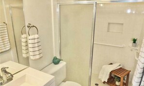 A bathroom with a glass shower enclosure, a toilet, a sink, and a small wooden stool with a plant. - Gorgeous 2-bedroom condo with AC in Long Beach two garages (Long Beach)
