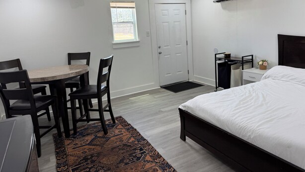 A bedroom with a bed, a desk with a chair, a small table with chairs, a window, and an air conditioning unit. - Studio Suite Near Ouachita River & Hot Springs (Malvern)