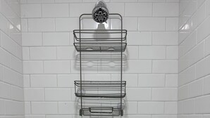 A shower area with white tiled walls, a showerhead, and a metal shelf unit. - Studio Suite Near Ouachita River & Hot Springs (Malvern)