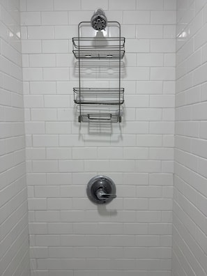 A shower area with white tiled walls, a showerhead, and a metal shelf unit.