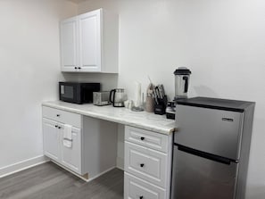 A compact kitchen with white cabinetry, a microwave, toaster, coffee maker, and a refrigerator.