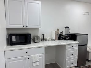 A kitchen with white cabinets, a microwave, toaster, coffee maker, blender, and refrigerator.