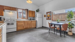 A kitchen with wooden cabinets, a white stove, a microwave, and a refrigerator. There is a dining table with chairs and a potted plant. - Guesthouse in Mendenhall Valley (Juneau)