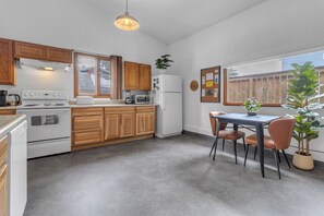 Une cuisine avec des meubles de rangement en bois, un fourneau blanc, un four à micro-ondes et un réfrigérateur. On y trouve une table à manger avec des chaises et une plante en pot.