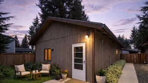 A wooden shed with a door, a small porch with chairs, and potted plants. - Guesthouse in Mendenhall Valley (Juneau)