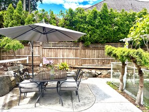 A patio with a table and chairs, an umbrella, and a wooden fence. - hot tub villa with a sauna room (Surrey)