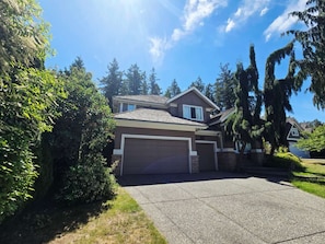 A two-story house with a garage, surrounded by greenery and trees. - hot tub villa with a sauna room (Surrey)