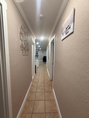 Un couloir aux murs de couleur beige, doté d’un sol carrelé et d’un plafond pourvu d’un éclairage encastré.