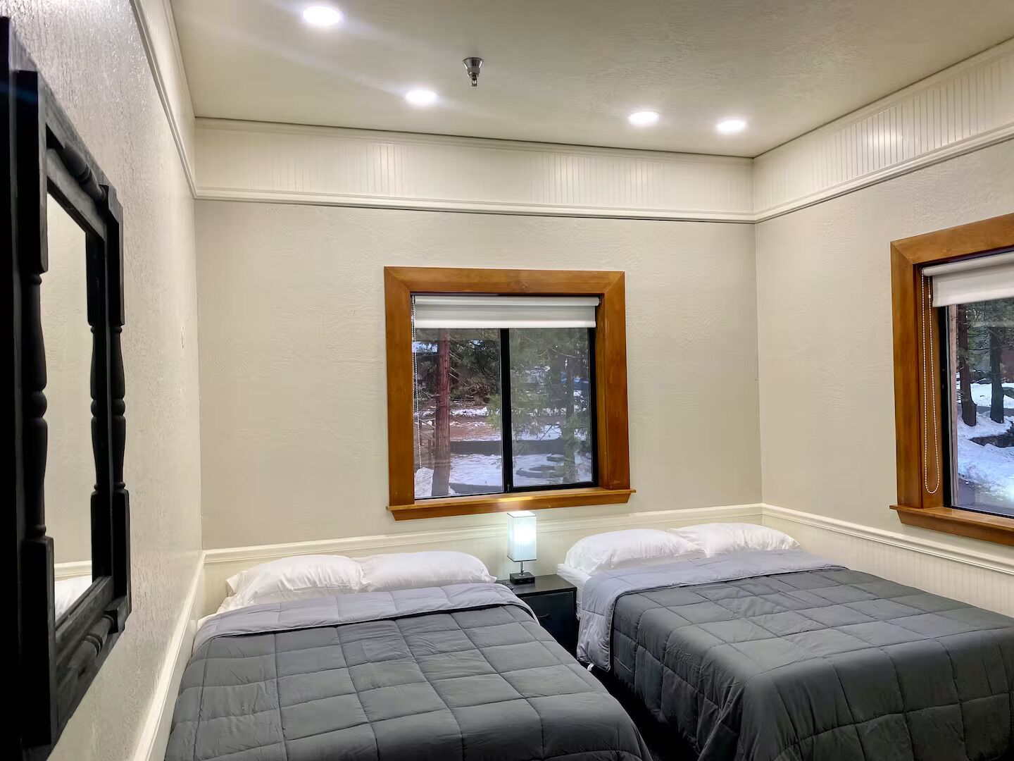 A room with two beds, a window with a view of trees, and a ceiling with recessed lighting.