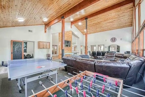 A room with a foosball table, a ping pong table, a sofa, and a conference table.