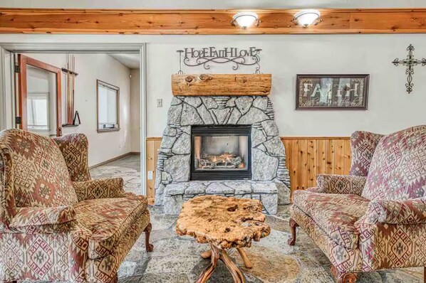 A cozy living room with patterned furniture, a stone fireplace, and a cross on the wall.