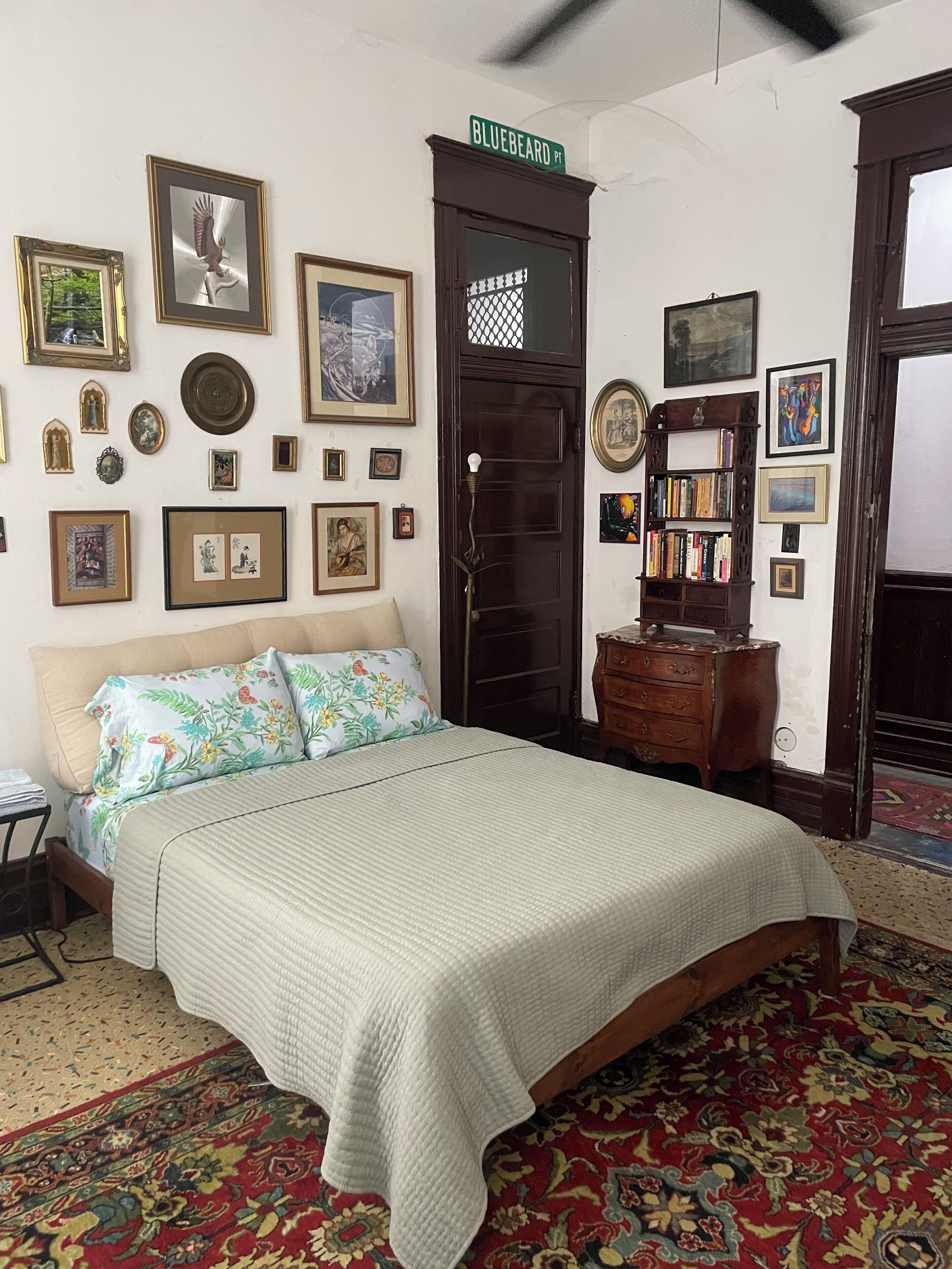 A bedroom with a bed, a dresser, a bookshelf, and various framed pictures on the walls.