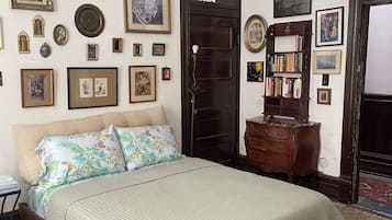 A bedroom with a bed, a dresser, a bookshelf, and various framed pictures on the walls.