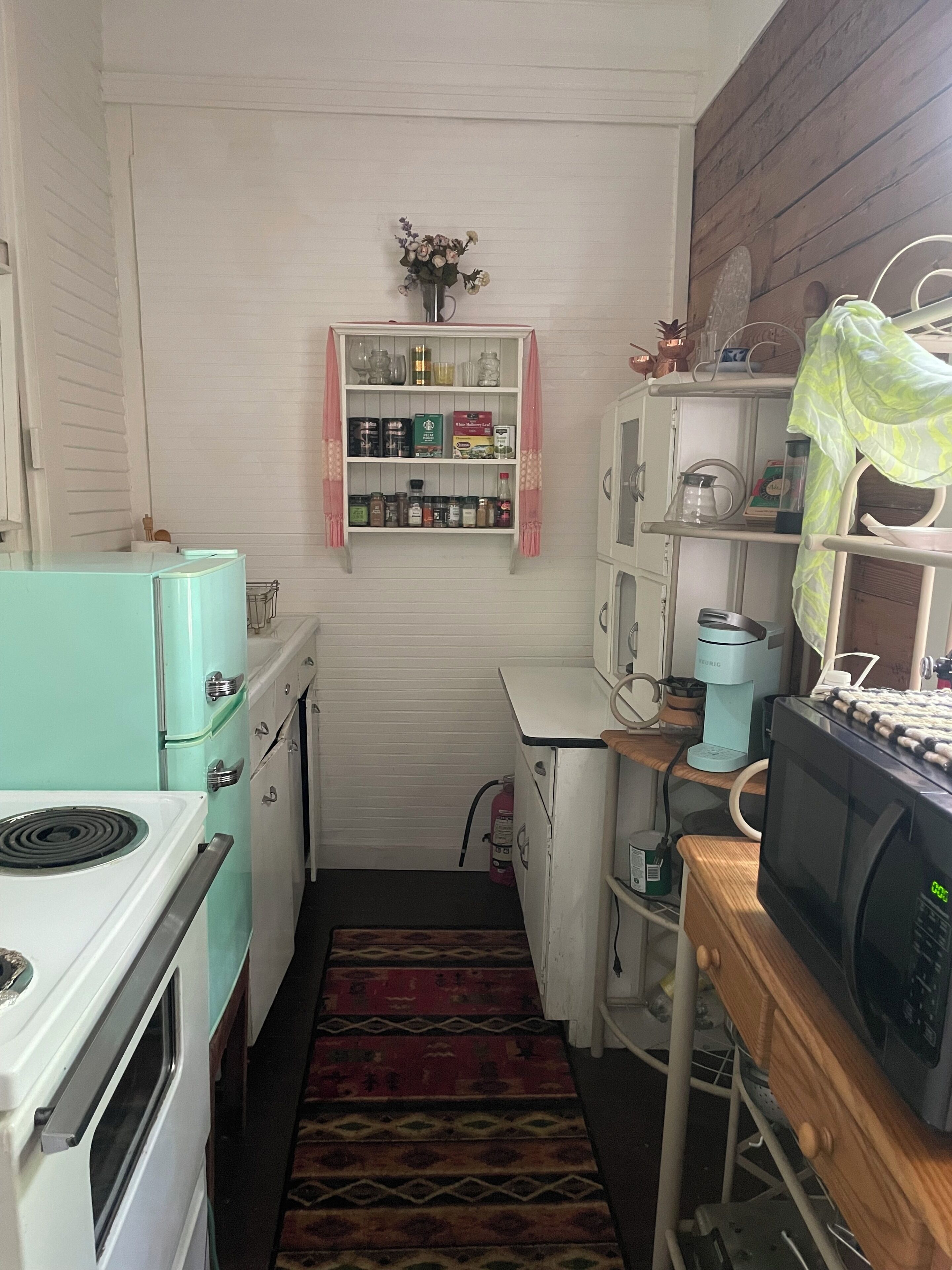 A compact kitchen with vintage appliances, a small pantry, and a microwave on a wooden counter.