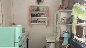Een compacte keuken met vintage apparatuur, een kleine voorraadkast en een magnetron op een houten aanrecht.