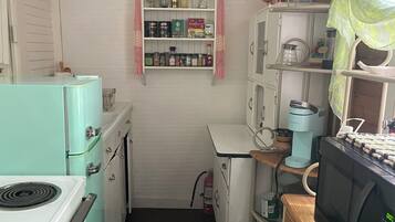 A compact kitchen with vintage appliances, a small pantry, and a microwave on a wooden counter.