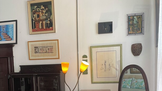 Een kamer met een houten kast, een spiegel en verschillende kunstwerken in lijsten aan de muur.