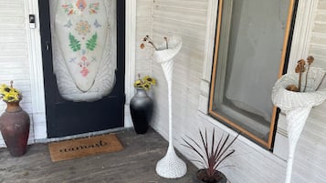 Un portico con una porta decorativa, una lampada da terra in vimini, un tappetino d'ingresso e un tappeto colorato.