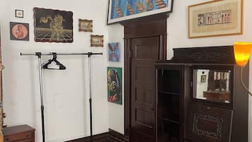 Una habitación con un armario de madera, una lámpara colgante, un tapete estampado y varias obras de arte enmarcadas en la pared.