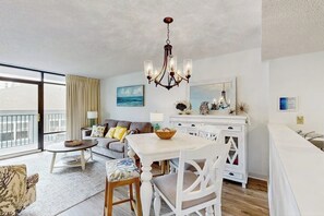 A modern living room with a dining area, a chandelier, and a view of the sea through large windows.