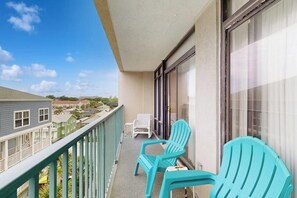 Un balcón con dos sillas turquesa, una silla blanca y vista a casas vecinas.