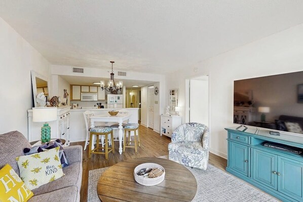 Una sala de estar con sofá, una mesa de centro, un mueble para televisión y una zona de comedor con mesa y sillas.
