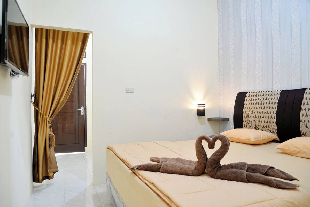 A hotel room with a bed, a wall-mounted light, a curtain, and a door.