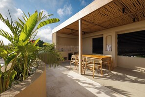A covered outdoor patio with a wooden table and chairs, surrounded by plants and a concrete floor. - SISI Wellness Villas (Pecatu)