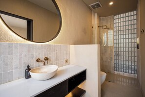 A bathroom with a large oval sink, a round mirror, and a shower with a glass door. - SISI Wellness Villas (Pecatu)