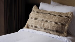 Una cama con ropa blanca, un cojín de tejido y una lámpara colgante de estilo bambú.