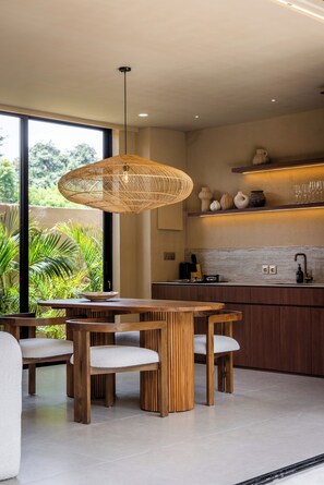 A modern kitchen with a dining area, large windows, and a hanging light fixture. - SISI Wellness Villas (Pecatu)