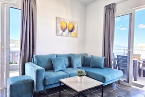 A modern living room with a blue sofa, a coffee table, and a painting on the wall. - Christine Sunny Corner 004 /w Sea View Balcony, Sarandë, Albania (Sarandë)