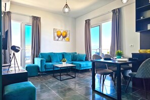 A modern living room with a blue sofa, a dining table, and a coffee table. - Christine Sunny Corner 004 /w Sea View Balcony, Sarandë, Albania (Sarandë)