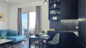 Ein stilvoller Wohnbereich mit Sofa, Esstisch, Stühlen, Küchenzeile und Blick durch ein großes Fenster.