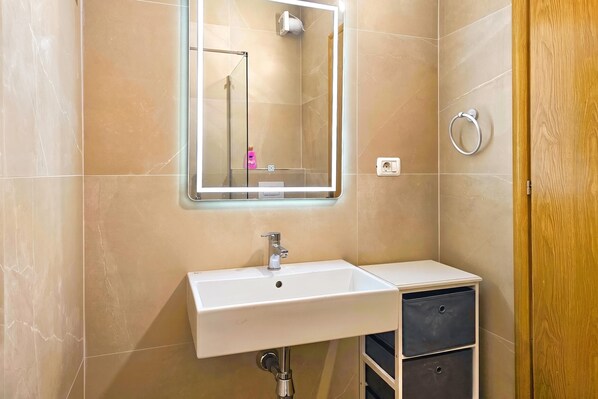 Une salle de bain avec un lavabo blanc, un miroir avec un éclairage intégré, un porte-serviettes et une porte en bois.