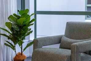 Ein Zimmer mit großem Fenster, einer Topfpflanze und einem gestreiften Sessel.