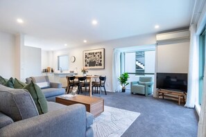 Ein modernes Wohnzimmer mit Sofa, Couchtisch, Fernseher, Essbereich und Wendeltreppe.