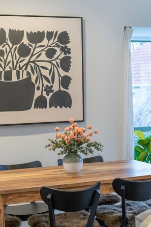 Ein Essbereich mit Holztisch, schwarzen Stühlen, einer Blumenvase und einem großen gerahmten Kunstwerk an der Wand.