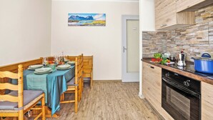 A compact kitchen with wooden cabinets, a dining table set for four, and a stone backsplash. - Francis Home with Balcony and Parking, Villaretto, Italy (Villaretto)