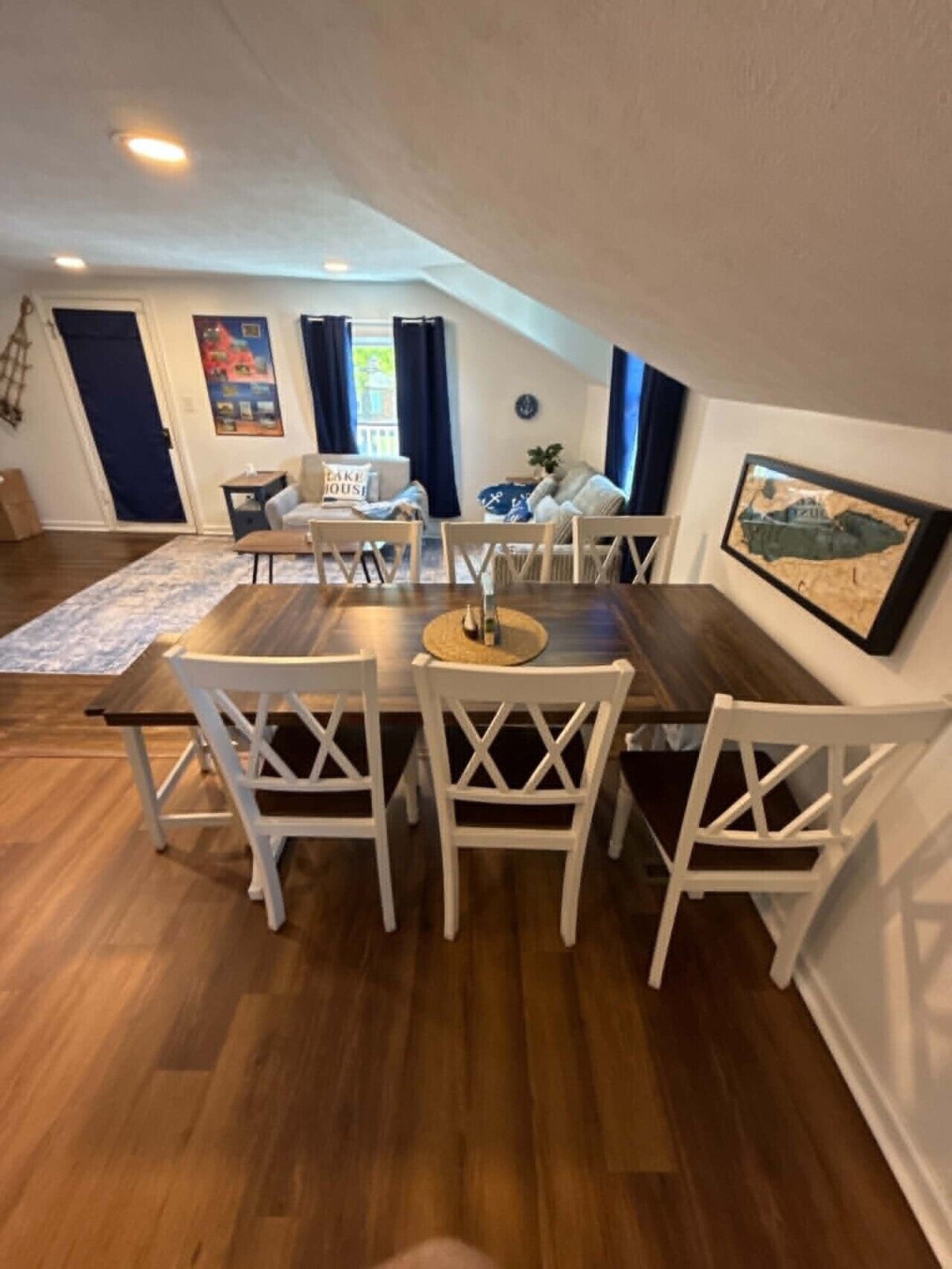 Ein Essbereich mit Holztisch und weißen Stühlen, einem blauen Vorhang und einem gerahmten Bild an der Wand.