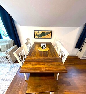 Una mesa de comedor con sillas, un tapete, un cuadro en la pared y una ventana con cortinas.