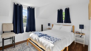 Quarto com cama, duas mesas de cabeceira, uma cadeira e janela com cortinas.